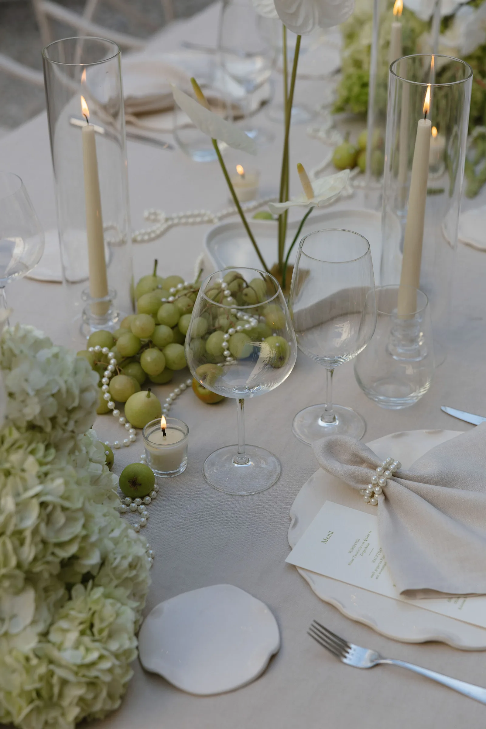 Hochzeitstisch mit weißen Blüten, Kerzen, grünen Trauben und Menükarte