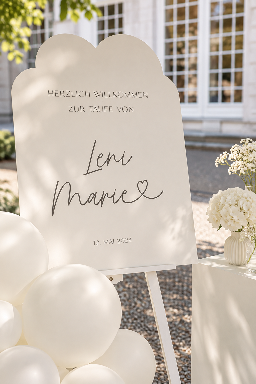 Wolkenförmiges Willkommensschild zur Taufe mit weißen Ballons und Blumen im Garten