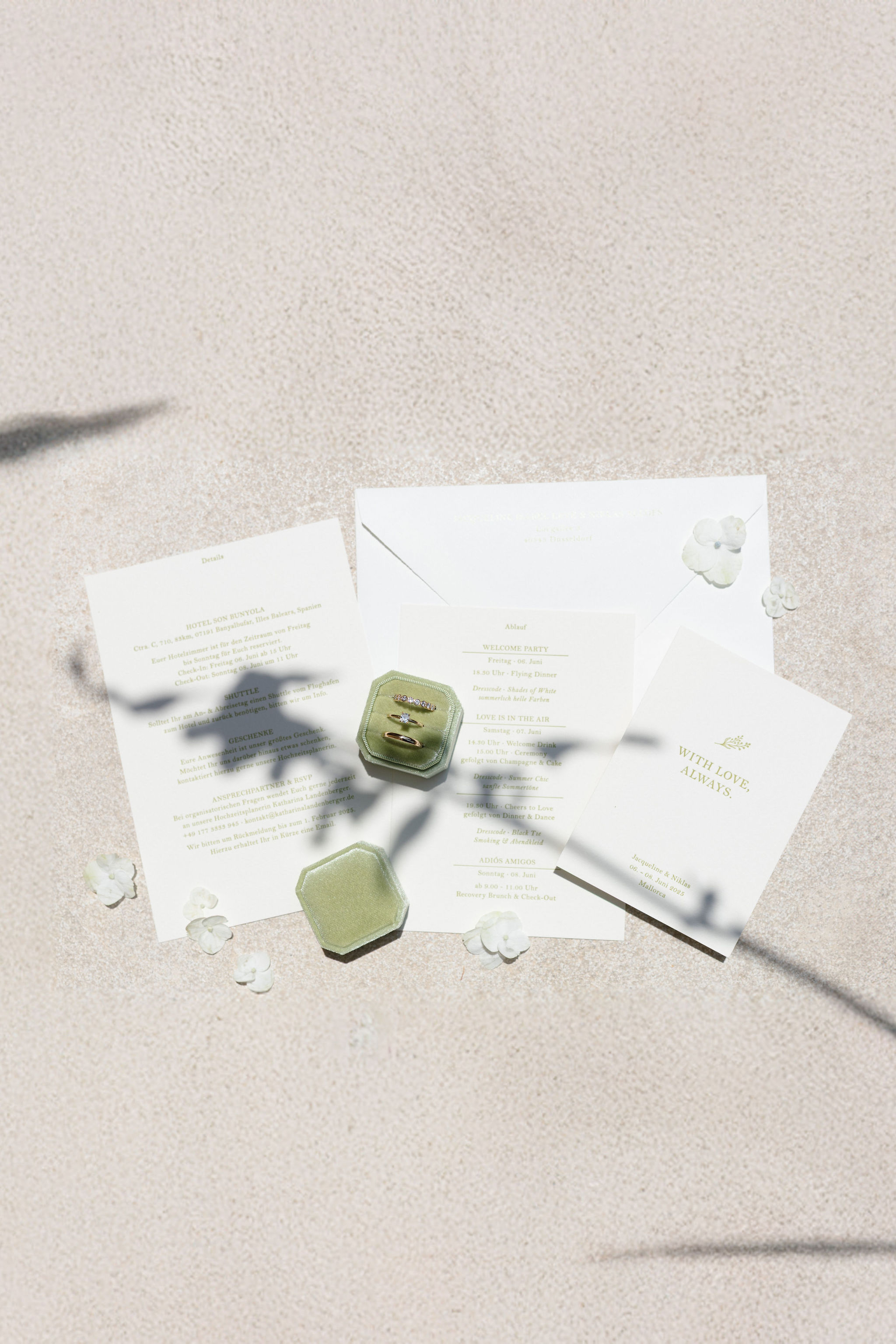 Hochzeitseinladungen mit grüner Schrift, Umschlag und Ringboxen im Sonnenlicht