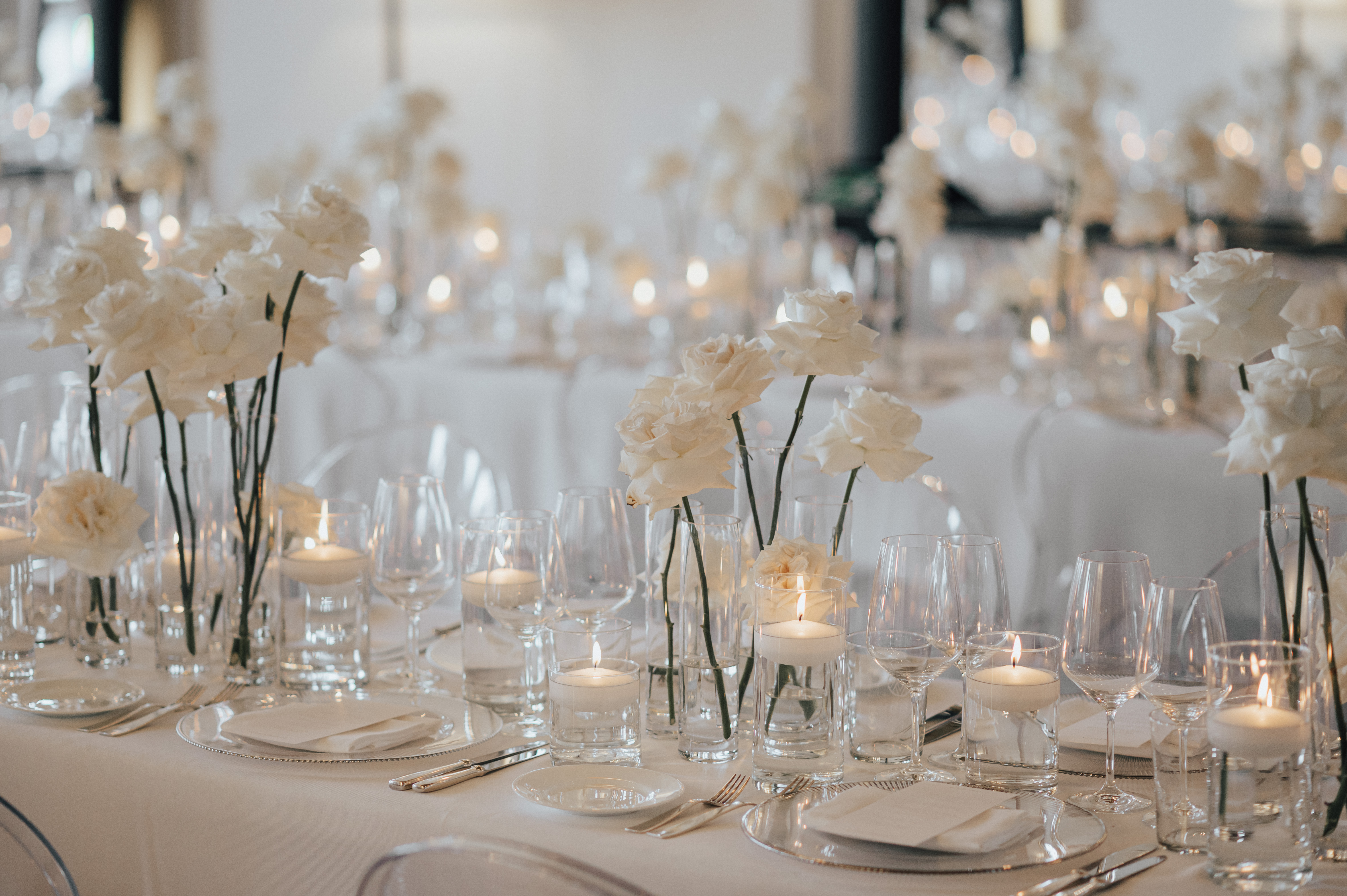 Hochzeitstafel mit weißen Rosen, Kerzen und Glasvasen